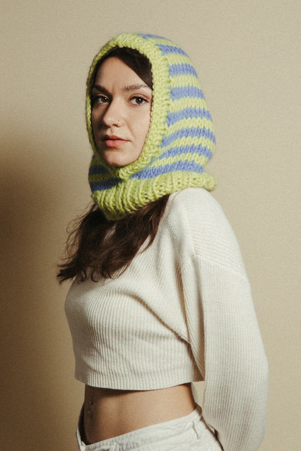 Woman wearing a green and blue striped knitted hood against a beige background
