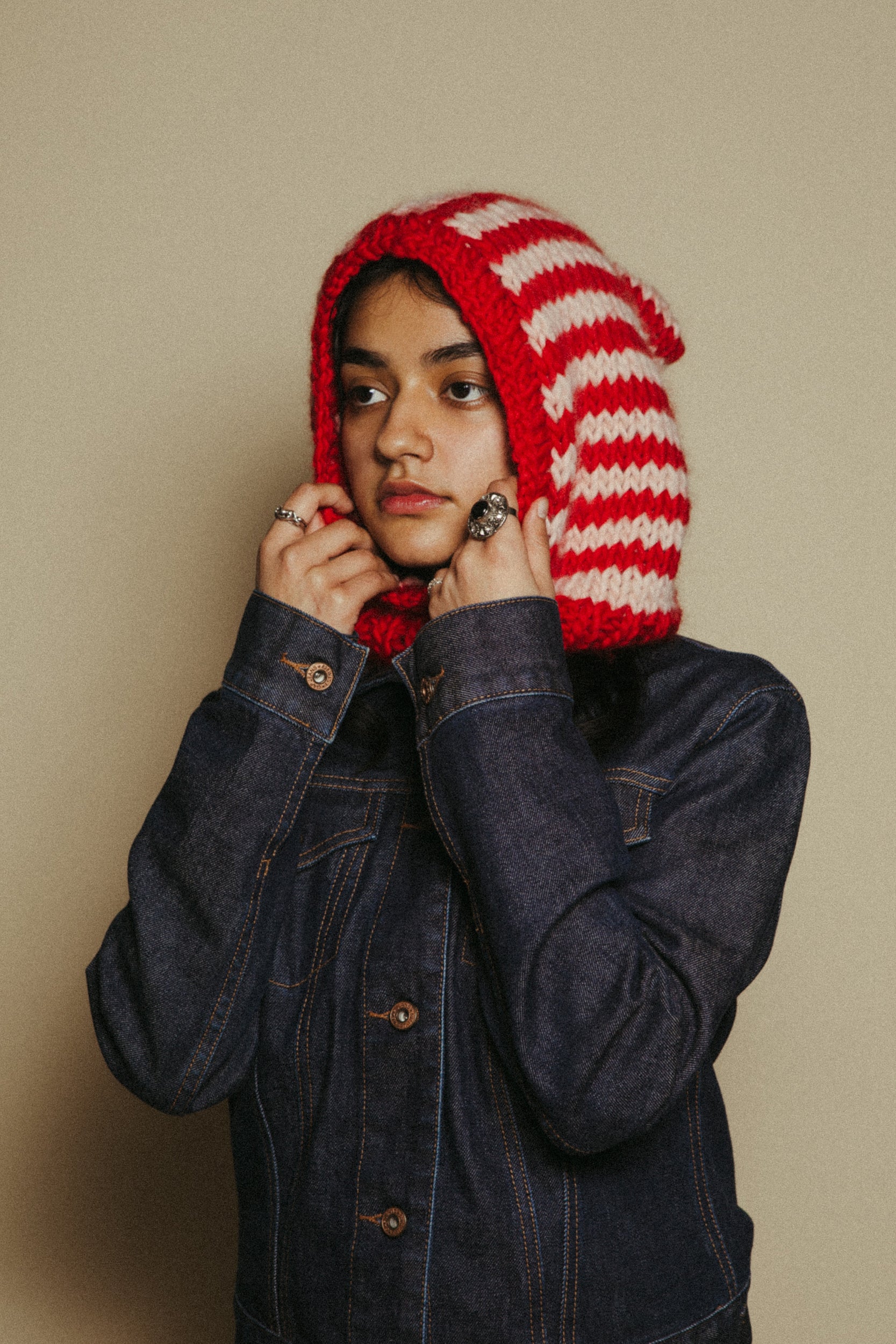 Person wearing a red and white striped knitted hood with a beige background