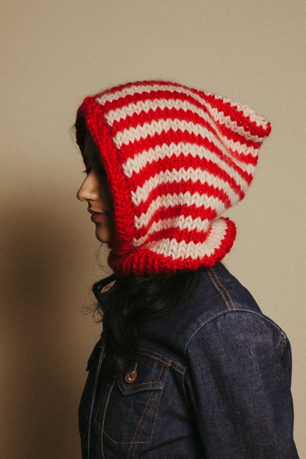 Person wearing a red and white striped knitted hood against a beige background
