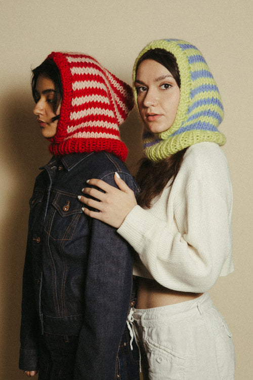 Two people wearing colorful knitted balaclava hoods against a beige background