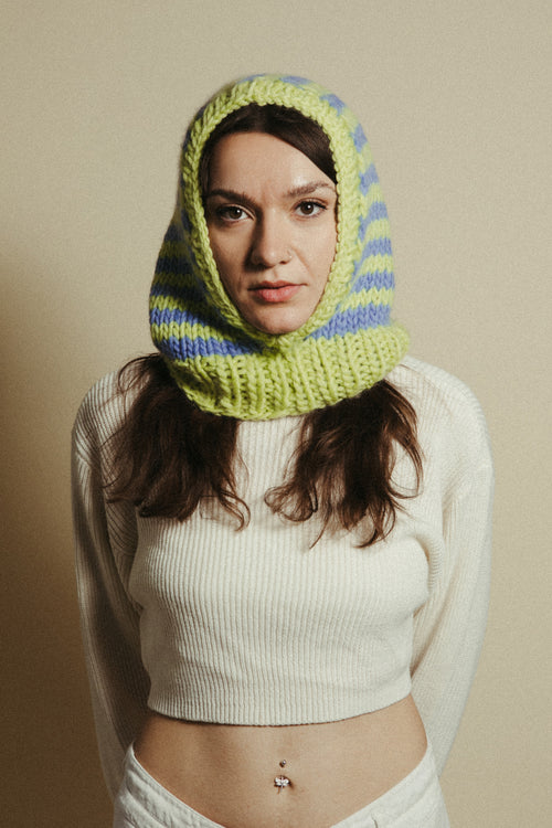 Woman wearing a green and blue knitted hood against a beige background