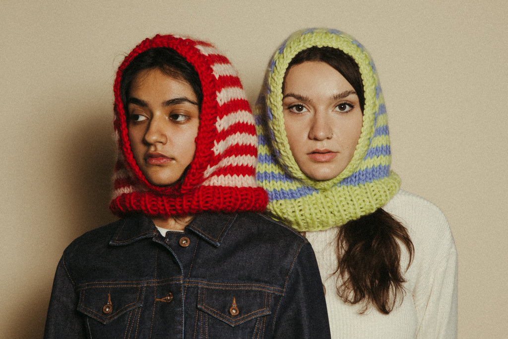 Two individuals wearing colorful knitted hoods against a plain background