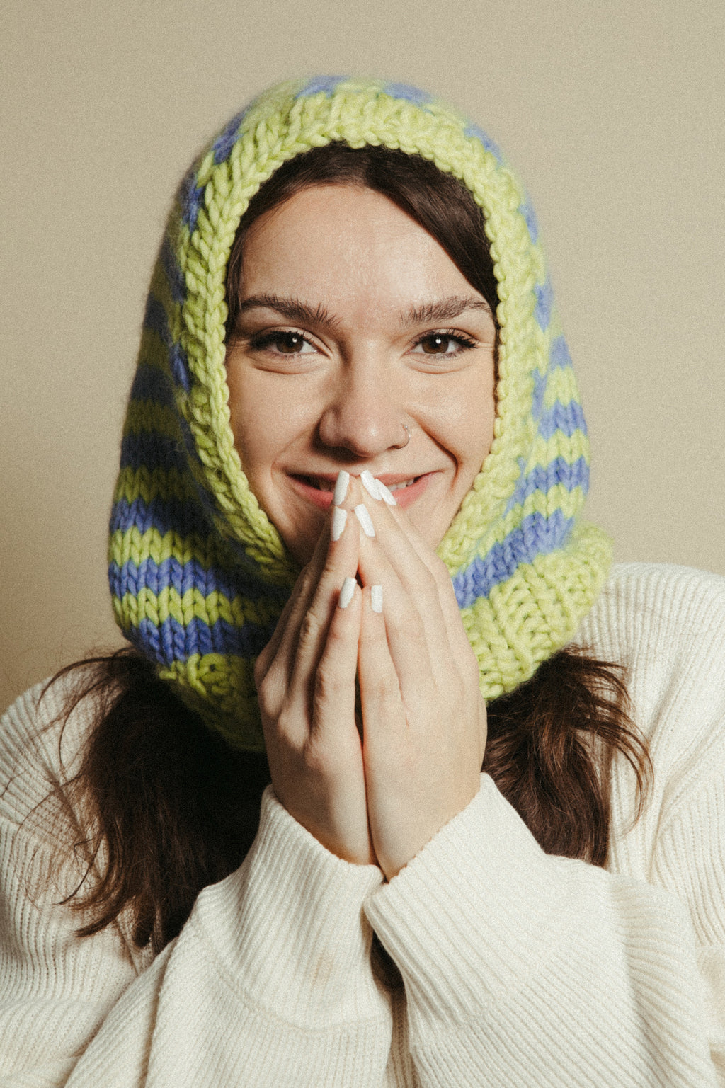Person wearing a green and blue striped knitted hood over their head, covering their ears.