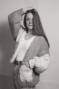 Person wearing a chunky knit cardigan against a plain background