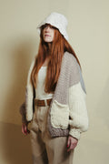 Woman wearing a chunky knit cardigan and white hat against a beige background