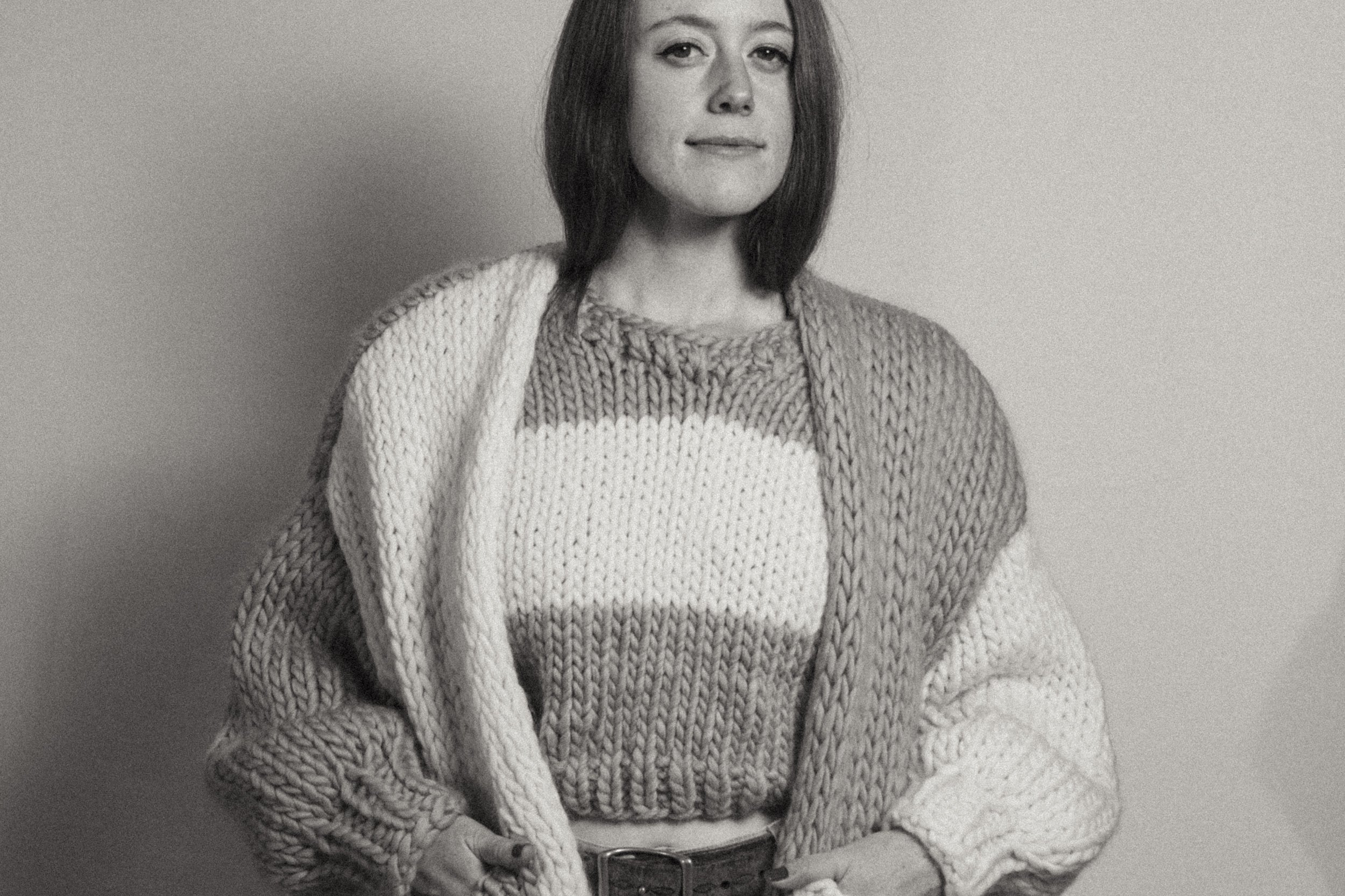 Black and white photo of a person wearing a knitted cardigan and sweater.