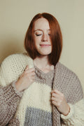 Woman wearing a chunky knit sweater with a neutral background
