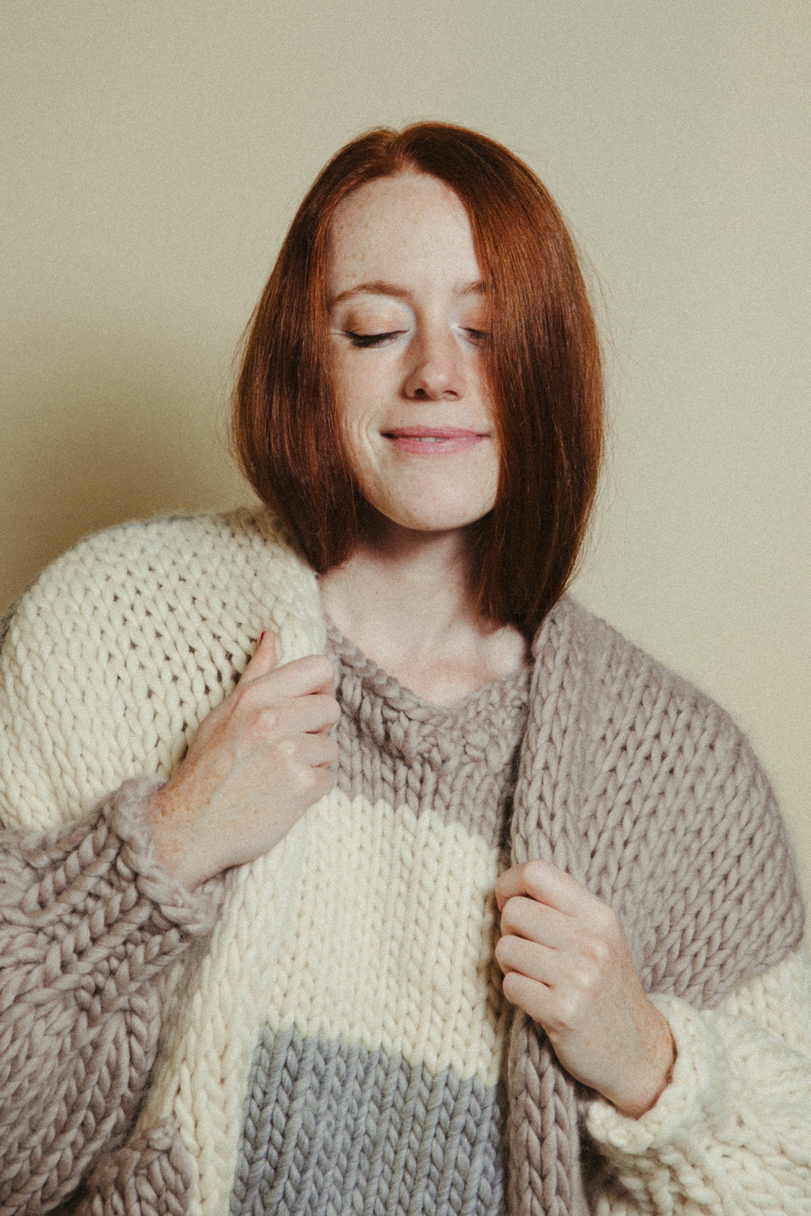 Woman wearing a chunky knit sweater with a neutral background