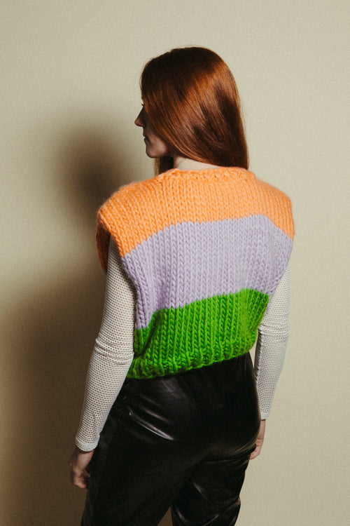 Person wearing a colorful knit sweater vest with an orange, lavender, and green pattern.