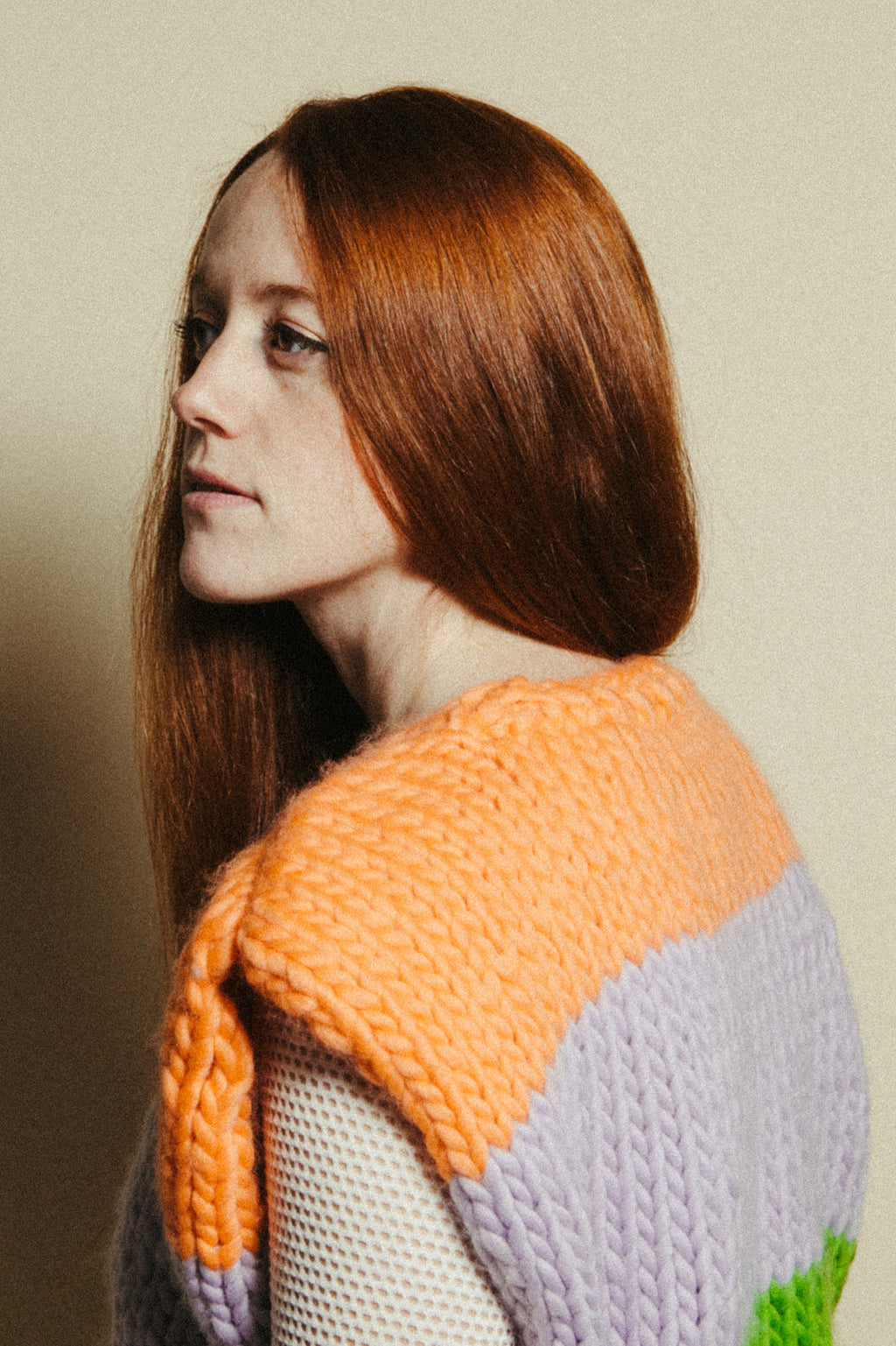Woman wearing a colorful knitted sweater vest with an orange, lavender, and green pattern on a beige background