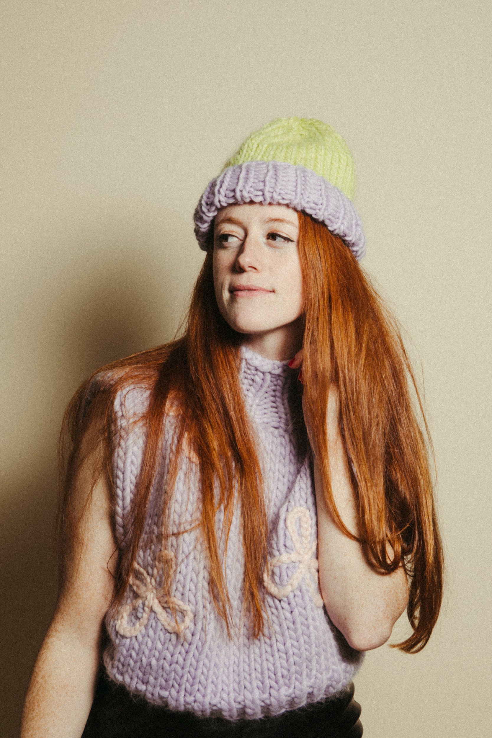 Person wearing a knitted hat and vest against a plain background