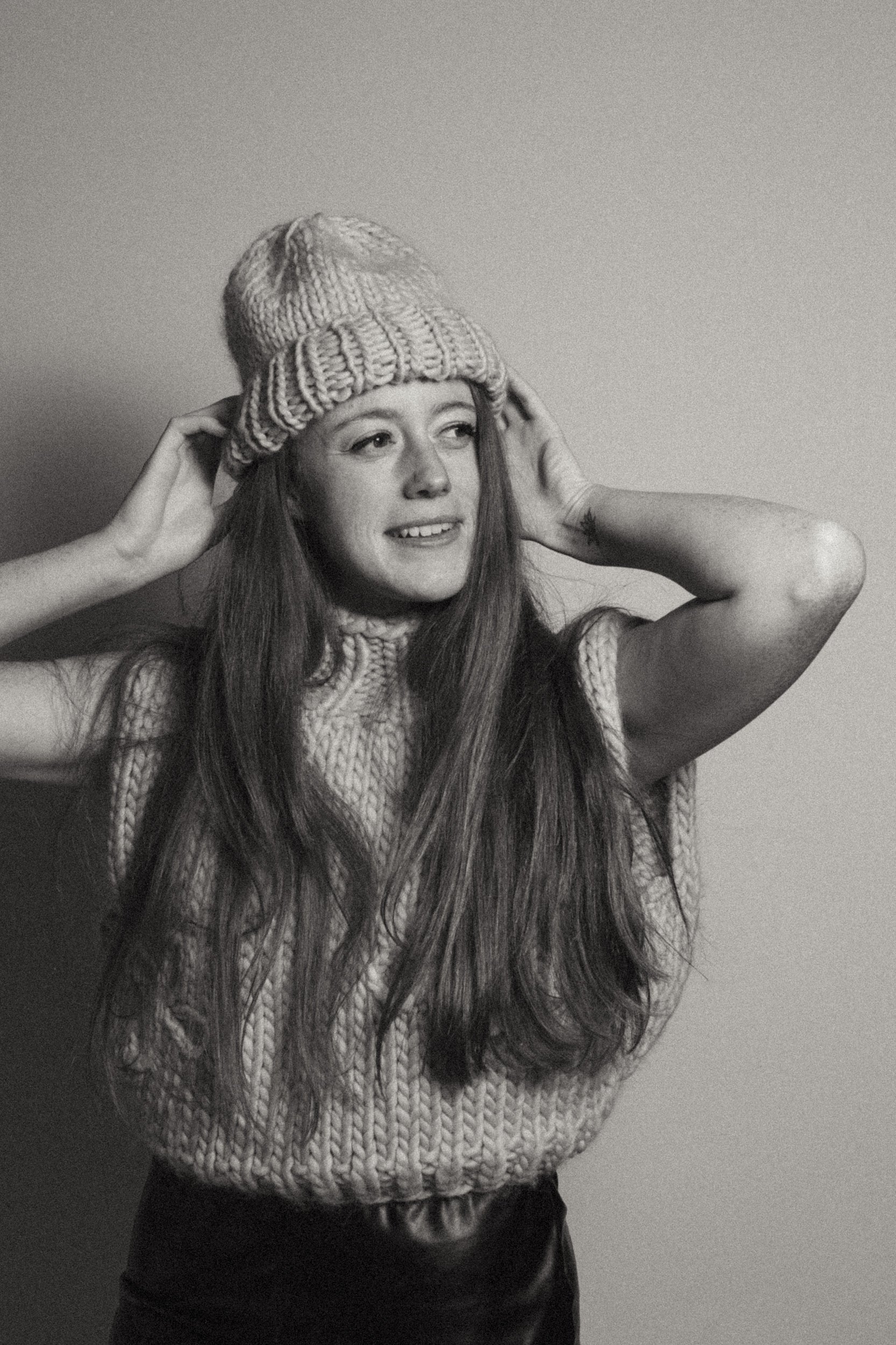 Person wearing a knitted hat and sweater against a plain background