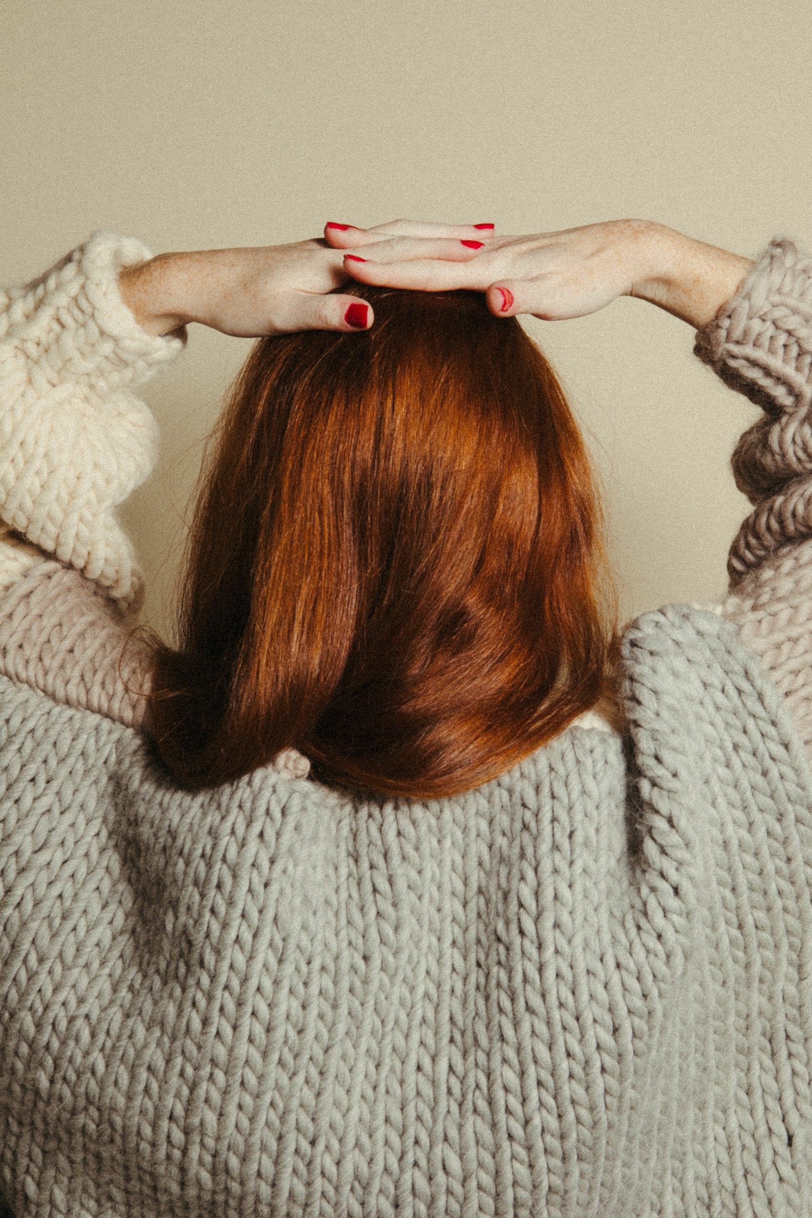 Person with red hair wearing a textured sweater against a neutral background