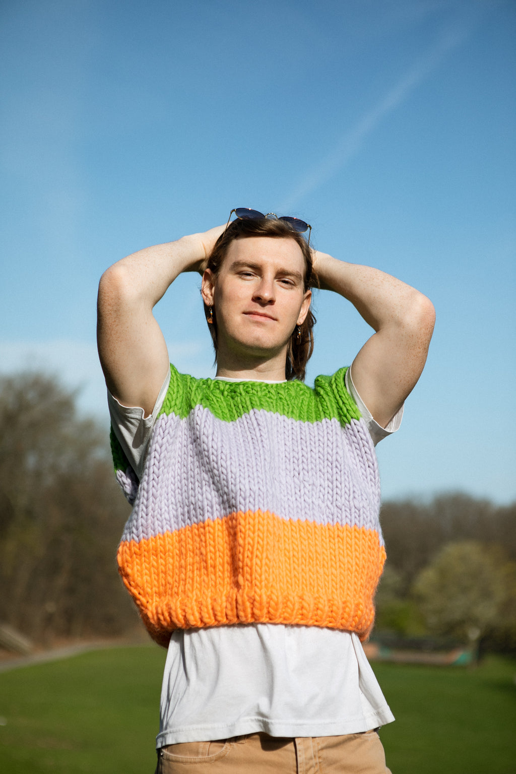Person wearing a colorful knitted sweater with a green, purple, and orange pattern outdoors.